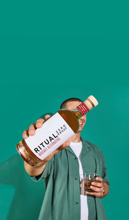 Person holding a bottle of Ritual whiskey against a teal background